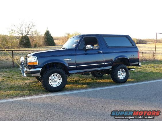 Blue lifted Ford Bronco parked on the side of a road, viewed from the side