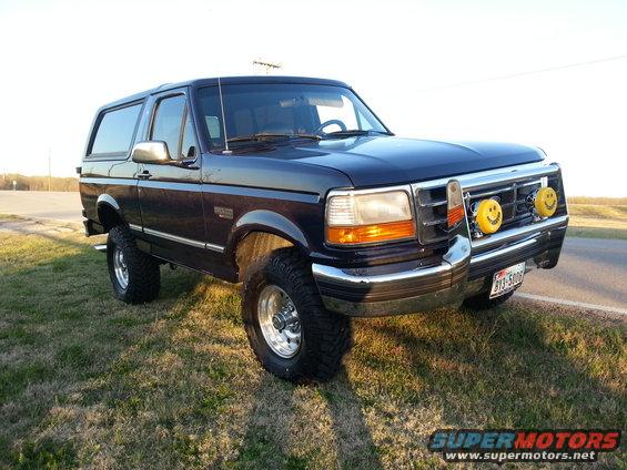 Dark blue 1995 Ford Bronco with smiley face fog lights and aftermarket wheels parked on grass