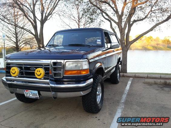 Blue Ford Bronco parked by a lake, has smiley face fog lights and a lifted suspension