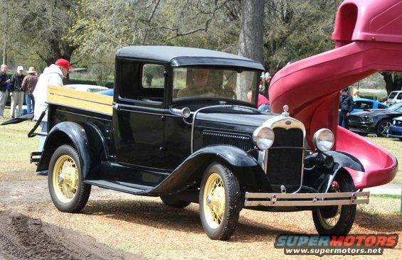 Black Ford Model A pickup truck with wooden bed, parked near a red slide. Other cars visible in background