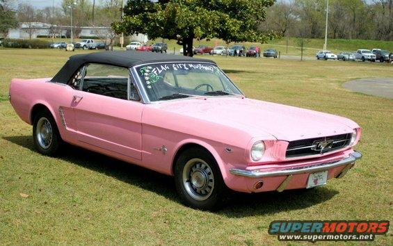 Pink convertible with black top, side view, parked on grass
