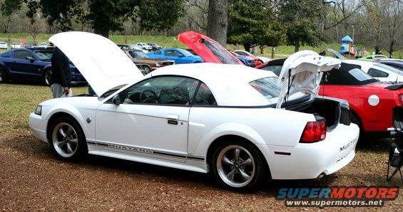 White convertible Mustang with hood and trunk open, parked outdoors with other cars