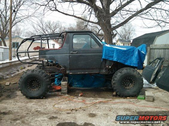 SUV with custom roll cage, large tires, and tarp covering front end, parked outside
