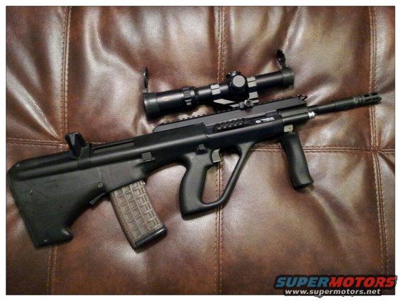 Assault rifle with scope mounted on top, resting on a brown leather surface