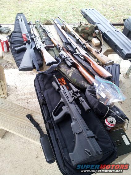 Multiple firearms and accessories laid out on a wooden table