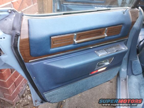 Interior of a car door with blue upholstery, wood trim, and chrome accents