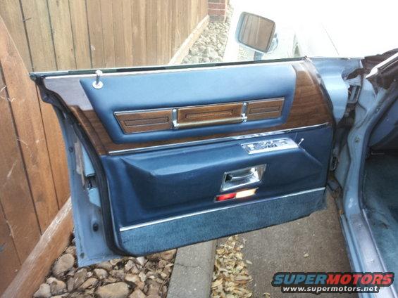 Interior of a car door with blue upholstery, wood trim, and chrome handle