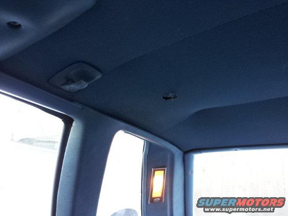 Interior shot of a car's blue headliner with a dome light and a hole in the ceiling. Window frames visible