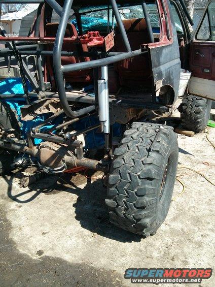 1986 Ford Bronco chassis with roll cage and large off-road tires, undergoing modification