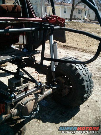 Modified off-road vehicle chassis with large tire, suspension, and roll cage. Red jack visible