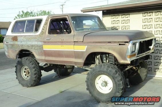 Modified 1978 Ford Bronco with large off-road tires and lifted suspension, parked outside a building