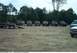 1993 Ford Bronco - A group of off-road vehicles are gathered in an open, dusty area with a treeline in the distance.