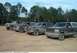 1993 Ford Bronco - Several Ford Broncos are lined up on a dirt track, with trees and flags visible behind them.