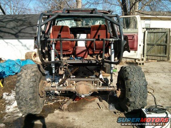 Rear view of heavily modified SUV with roll cage, large off-road tires, and exposed suspension