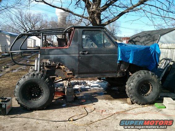Custom off-road SUV with large tires, roll cage, and tarped front end, sitting on blocks