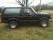 1987 Ford Bronco - Side view of a black Ford Bronco parked on a grassy area with trees in the background.