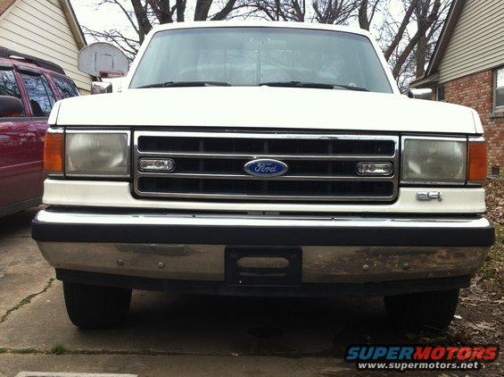 Front view of a white 1990 Ford F-150 parked in a driveway. Another vehicle is partially visible to the left