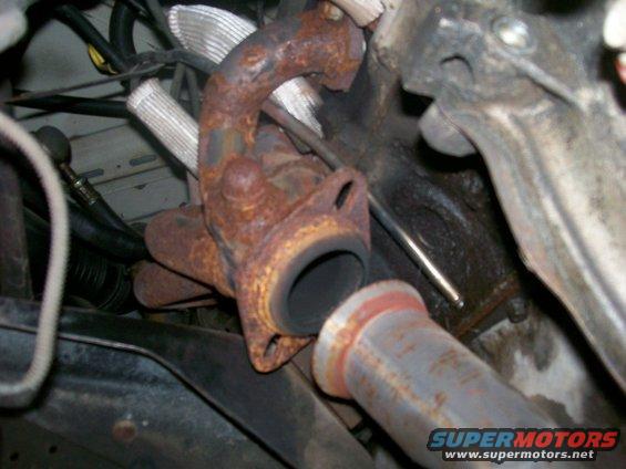 Rusted exhaust manifold connected to a pipe, with engine components visible