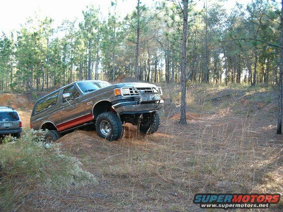 Gray Ford Bronco with red stripe, lifted, on dirt mound, front wheels turned left