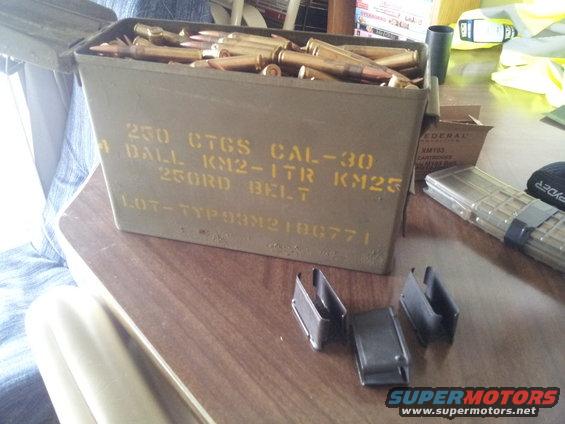 Ammo can filled with cartridges, plus some magazines and clips on a table
