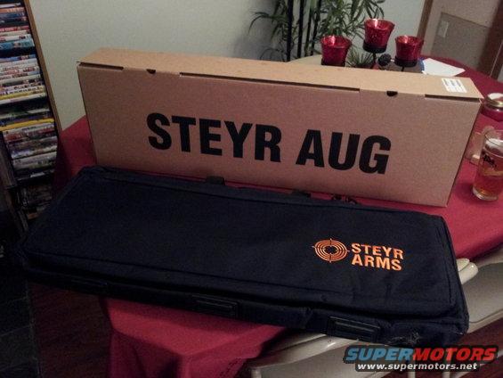 Cardboard box labeled STEYR AUG and a black gun case with STEYR ARMS logo on a table
