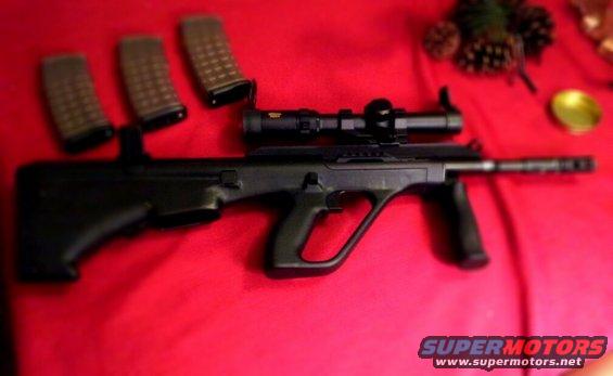 Bullpup rifle with scope and three magazines on red fabric