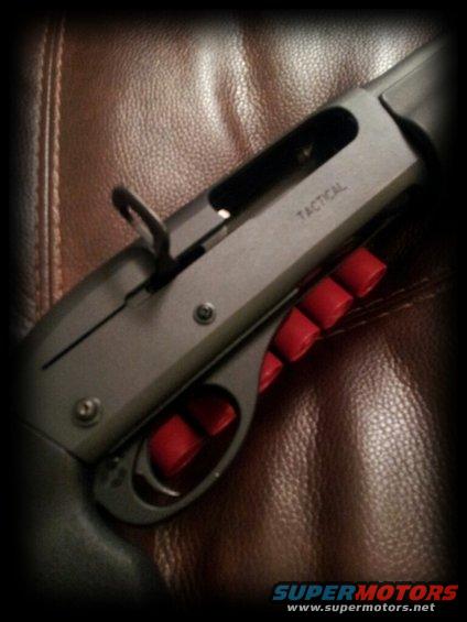 Close-up of a tactical shotgun receiver with red shell holders visible. Text 'TACTICAL' is engraved on the receiver