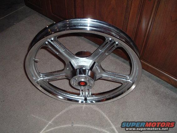 Chrome five-spoke motorcycle wheel with red accents on the hub, resting on carpet