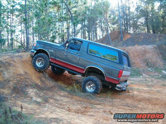 Gray and red Ford Bronco climbing a dirt hill, lifted suspension, off-road tires