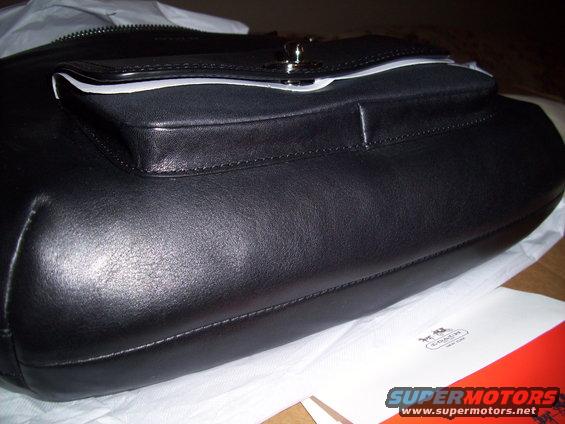 Black leather handbag with a front flap pocket and silver clasp, resting on white tissue paper with a Coach logo