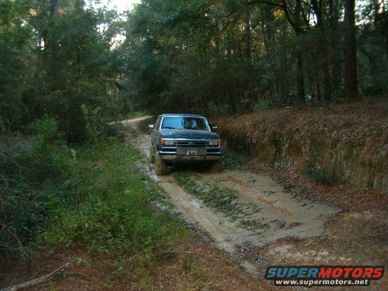 Dark blue 1992 Ford Bronco driving on a muddy forest road
