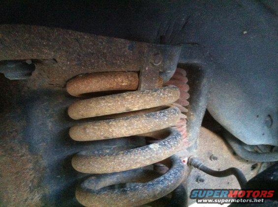 Rusty suspension coil spring with red shock absorber boot, close-up view of vehicle undercarriage