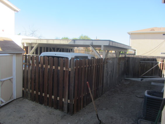 White van parked under a carport, partially obscured by a wooden fence