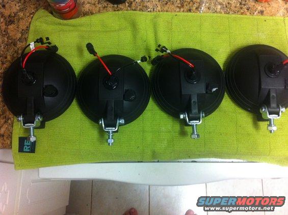Four black Hella 500 HID lights with red and black wiring on a green towel