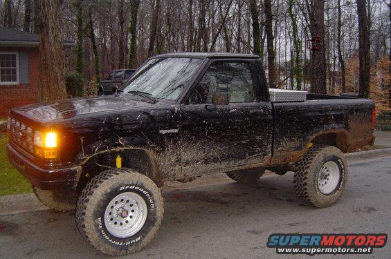 Mud-covered 1989 Ford Ranger pickup truck parked on a street, with another vehicle visible in the background