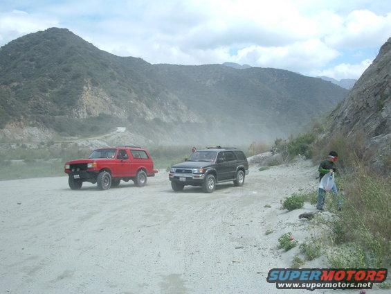 red Ford Bronco and black Toyota 4Runner on dirt road with mountains behind