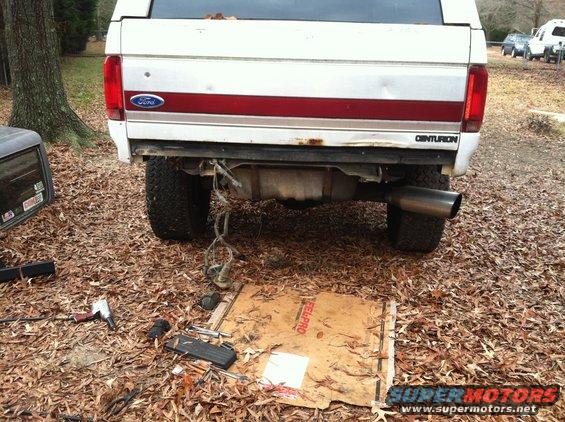 Rear of a white Ford Bronco Centurion Conversion with a large exhaust pipe and tools on the ground