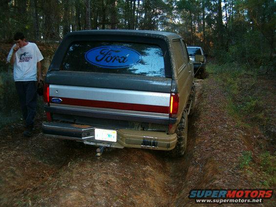 Rear view of a 1991 Ford Bronco on a dirt trail, with another vehicle behind it. A man stands to the left