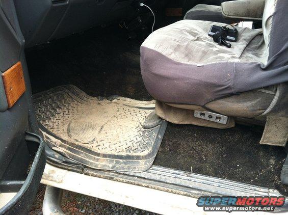 Interior shot of a dirty van or truck cab, showing a worn driver's seat and floor mats