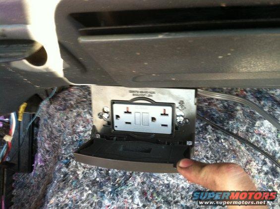 Interior view of a vehicle's exposed insulation and an aftermarket electrical outlet with two receptacles