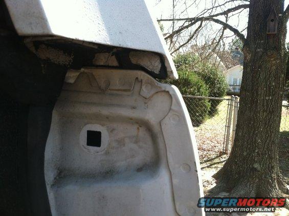 Close-up of a white vehicle's fender well, showing some dirt and damage