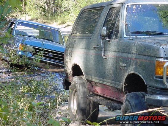 1991 Ford Bronco and a blue Ford truck stuck in mud off-road