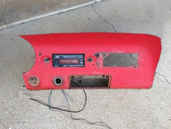Red car dashboard section with aftermarket cassette player installed, wires hanging