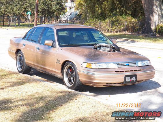 Modified Ford Crown Victoria with exposed engine sticking out of the hood, seen from the front-right