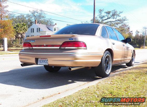Gold sedan rear view with custom wheels and spoiler. License plate reads 10IKVIC