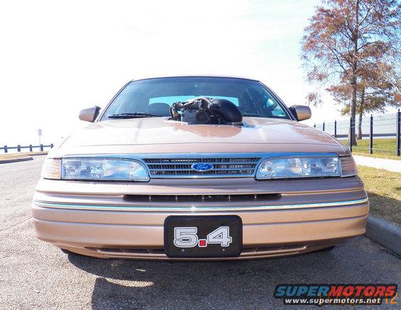 Front view of a tan Ford Crown Victoria with a large engine intake protruding from the hood and a '5.4' license plate
