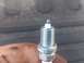 2004 Dodge 1500 - A single spark plug is shown, held by a hand with dirt smudges. The background is out of focus.