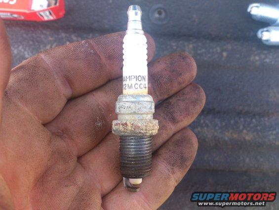 Hand holding a used Champion spark plug with "CHAMPION 2M CC4" visible