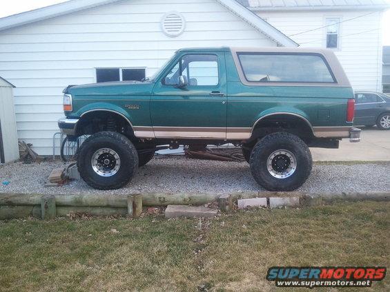 Side view of a lifted green 1996 Ford Bronco with a tan top and large off-road tires