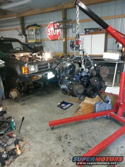 Car in garage with engine hoist lifting out the motor. Front end of car visible